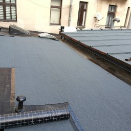 PATRYK FLORSZ - Widok z góry na płaski dach pokryty nową papą termozgrzewalną, z widocznym rolką materiału Swissopor Bikutop i detalami konstrukcyjnymi dachu w tle.