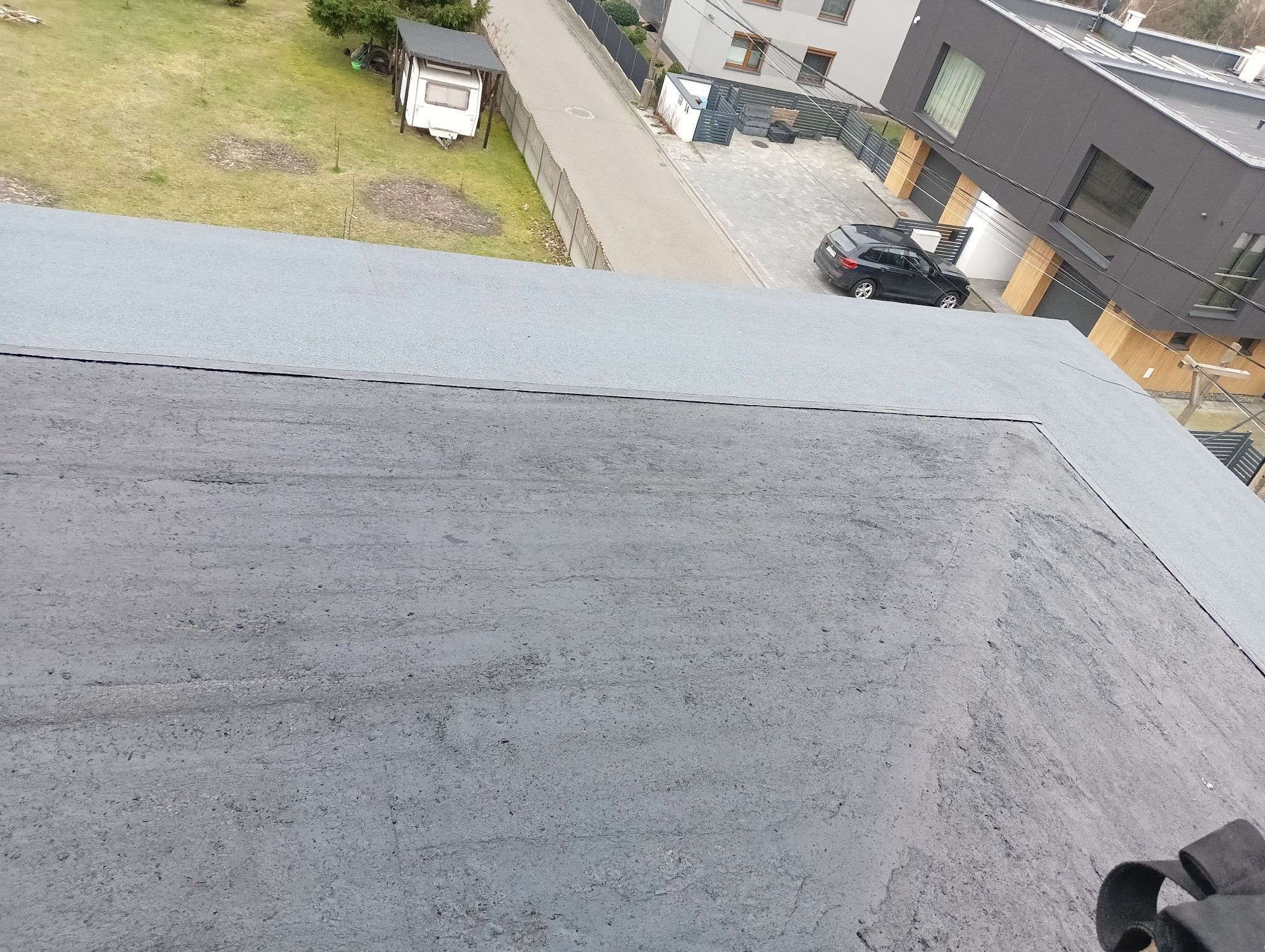 Powierzchnia bitumiczna dachu płaskiego po renowacji, widok z góry na tle zieleni i zabudowy miejskiej.