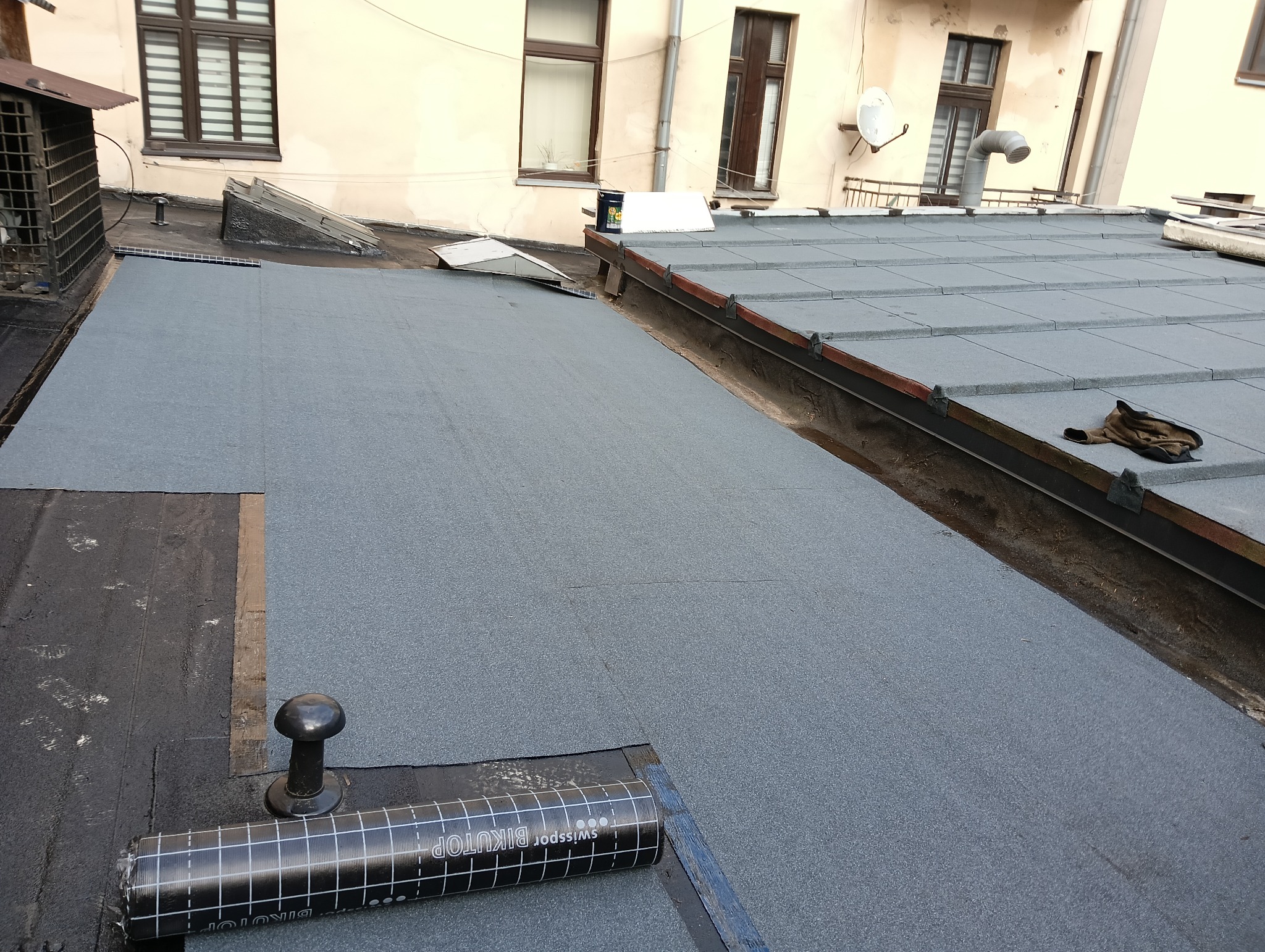 Widok z góry na płaski dach pokryty nową papą termozgrzewalną, z widocznym rolką materiału Swissopor Bikutop i detalami konstrukcyjnymi dachu w tle.