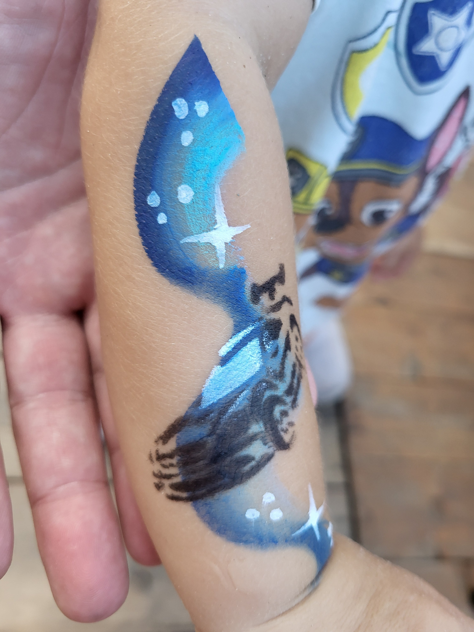 Ręka dziecka z namalowanym na skórze motywem z bajki, dominują odcienie niebieskiego i białe gwiazdki.