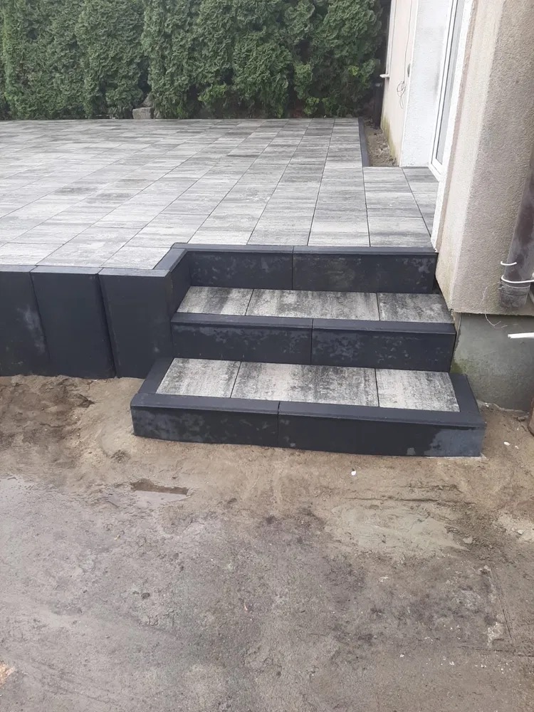 Schody z kostki brukowej prowadzące na taras, widoczne niedokończone prace ziemne wokół.