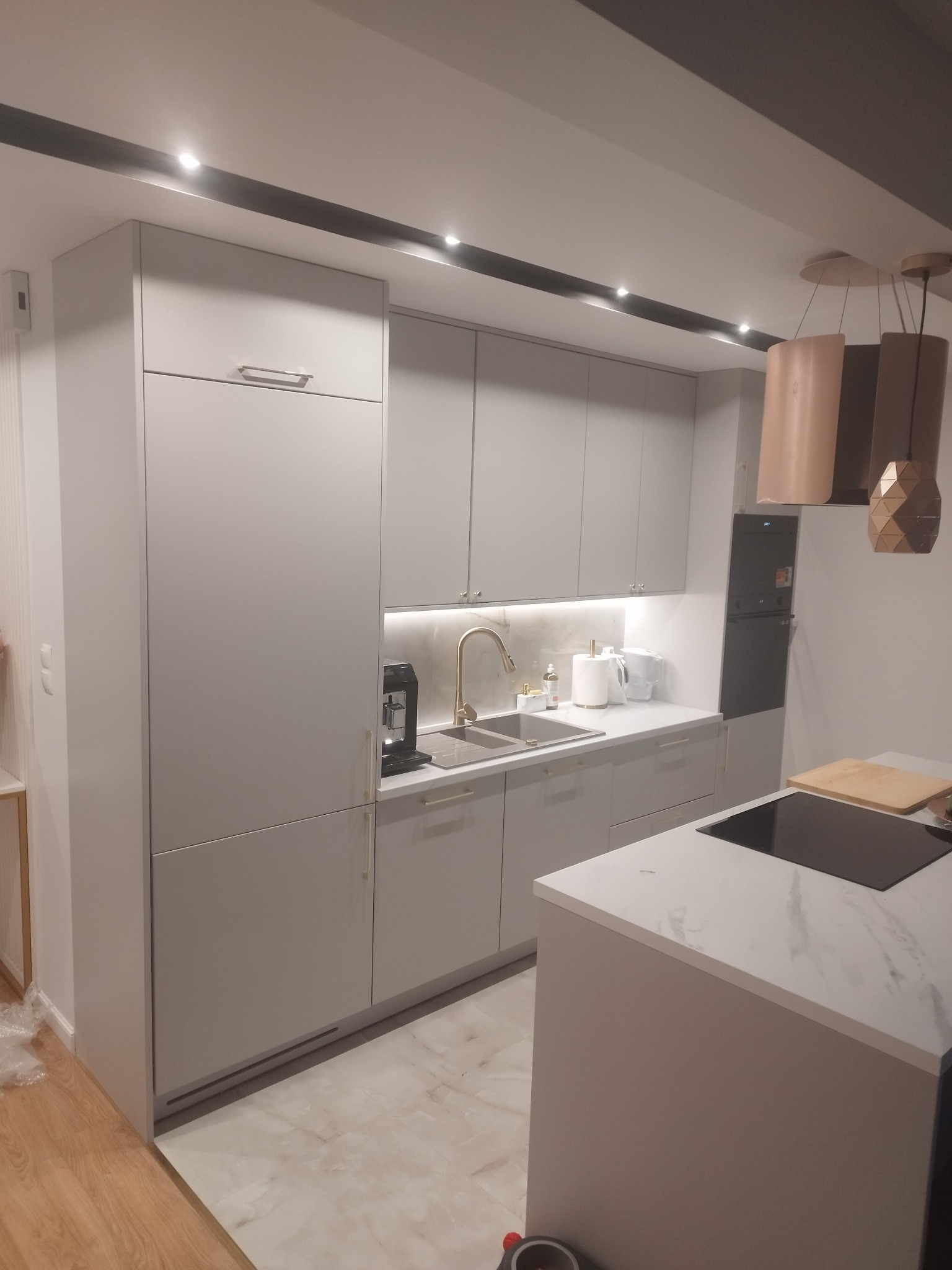 Szara kuchnia na wymiar z wyspą, złota armatura, zabudowa po sufit, marmurowy blat i podłoga.