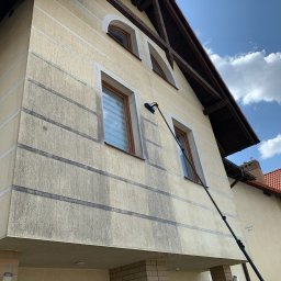 KONKRET Tomasz Augustyniak - Dwupiętrowy dom z elewacją w trakcie czyszczenia za pomocą szczotki na długim wysięgniku; widoczne zacieki i różnica w kolorze między czystą a brudną powierzchnią.