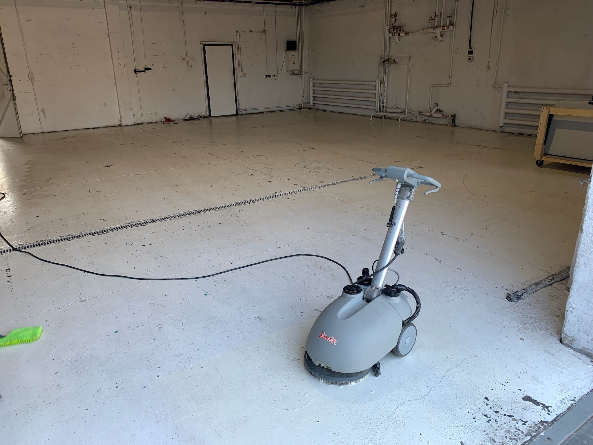 Szorowarka automatyczna Vipa 35E czyszcząca białą posadzkę w dużym, pustym pomieszczeniu przemysłowym z widocznymi instalacjami na ścianach.