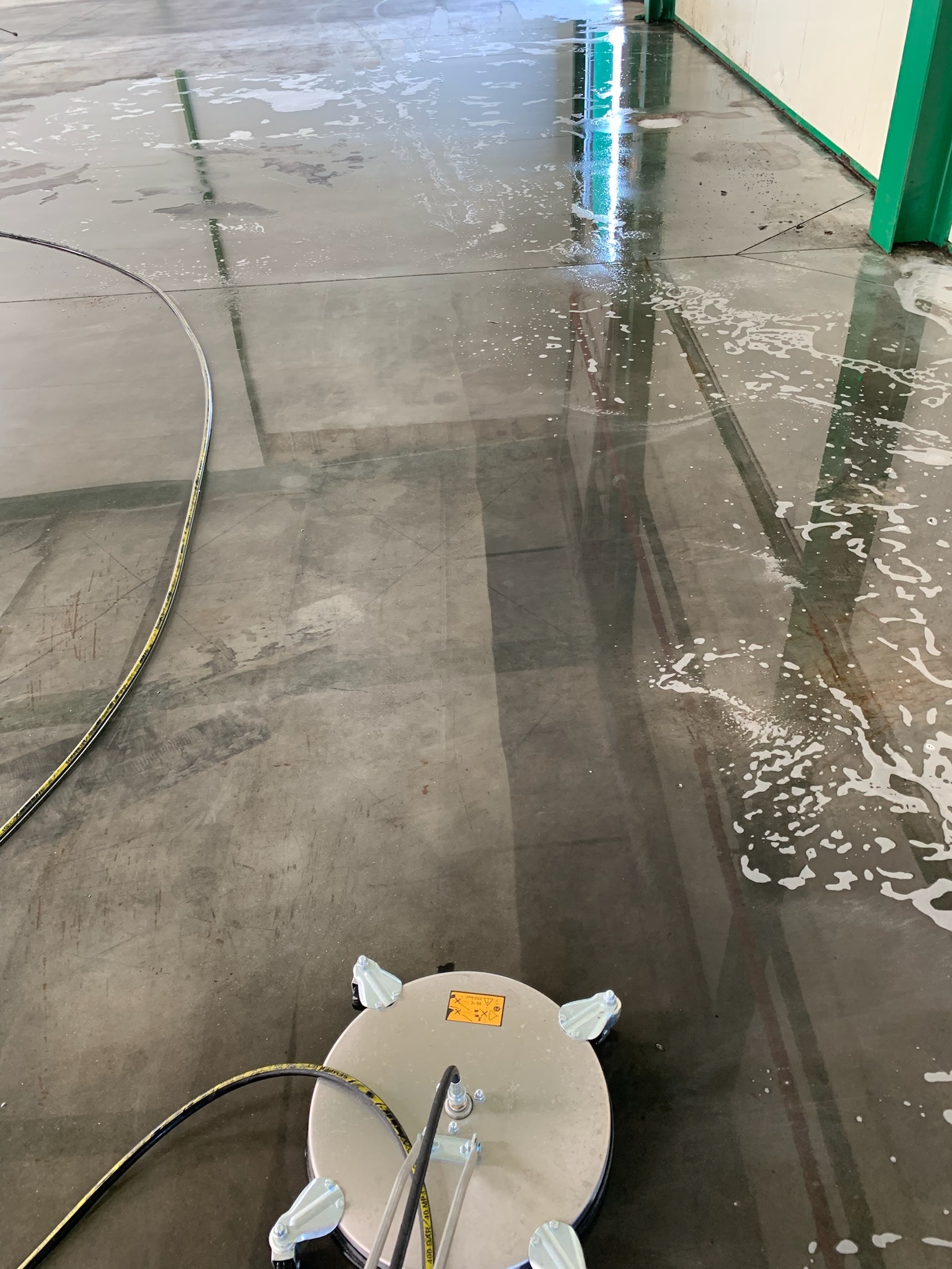 Szorowarka przemysłowa w trakcie pracy, czyszcząca posadzkę w hali, widoczne ślady po czyszczeniu i pozostałości piany.