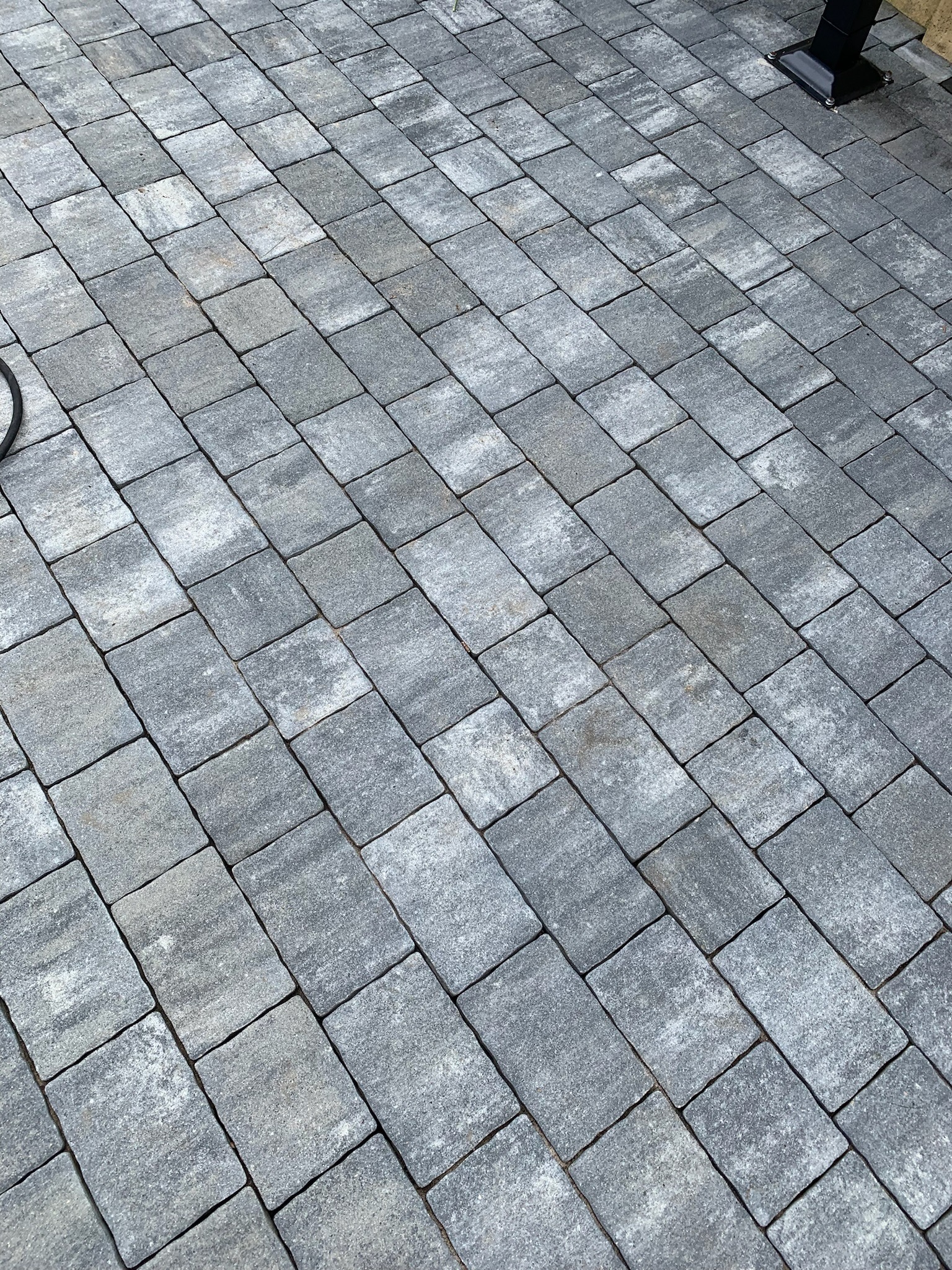 Ułożona szara kostka brukowa, widoczna z góry pod kątem, z elementami instalacji w tle.