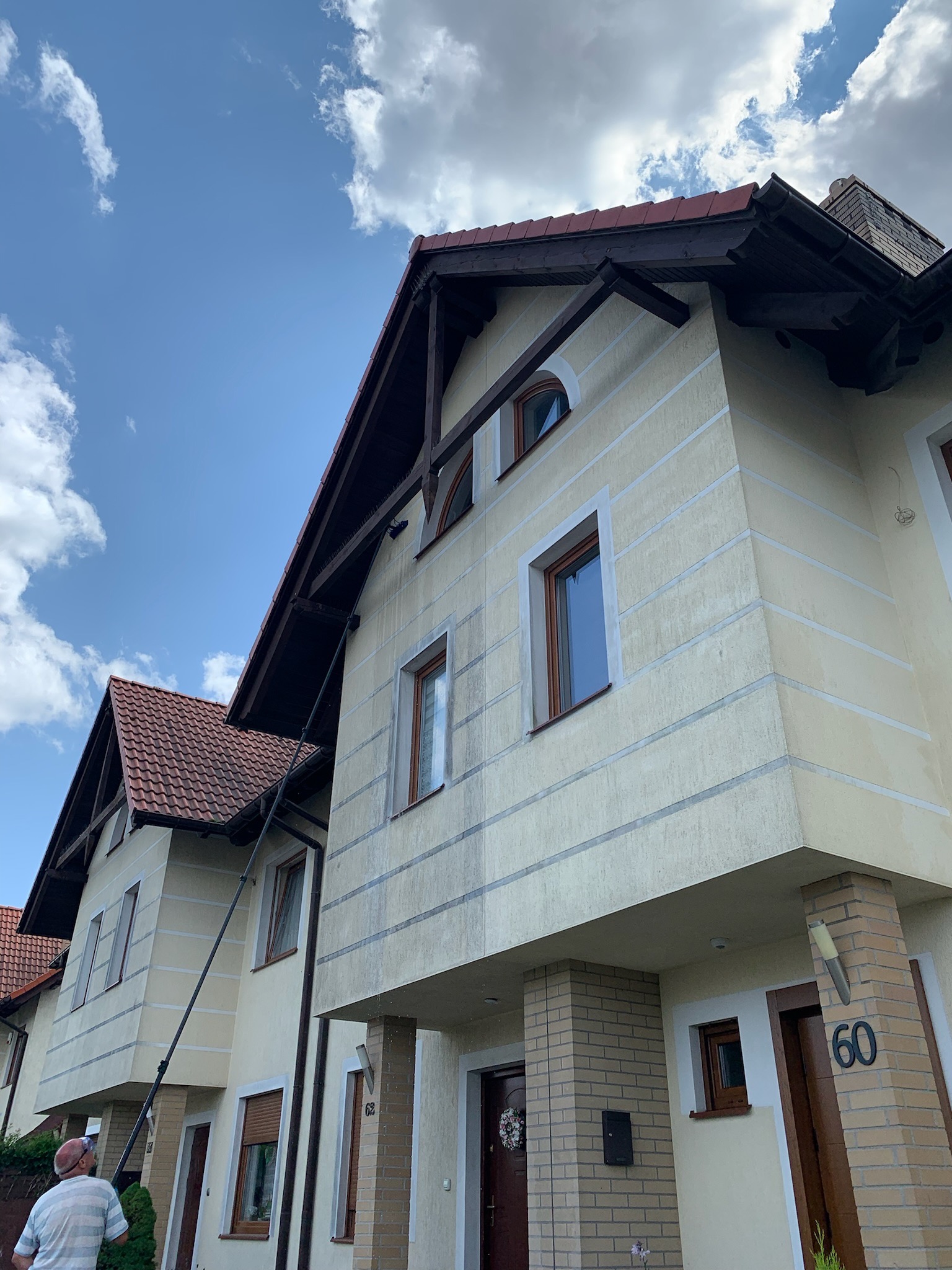 Czyszczenie elewacji domu jednorodzinnego z użyciem lancy teleskopowej, widoczne różnice w czystości powierzchni przed i po zabiegu.