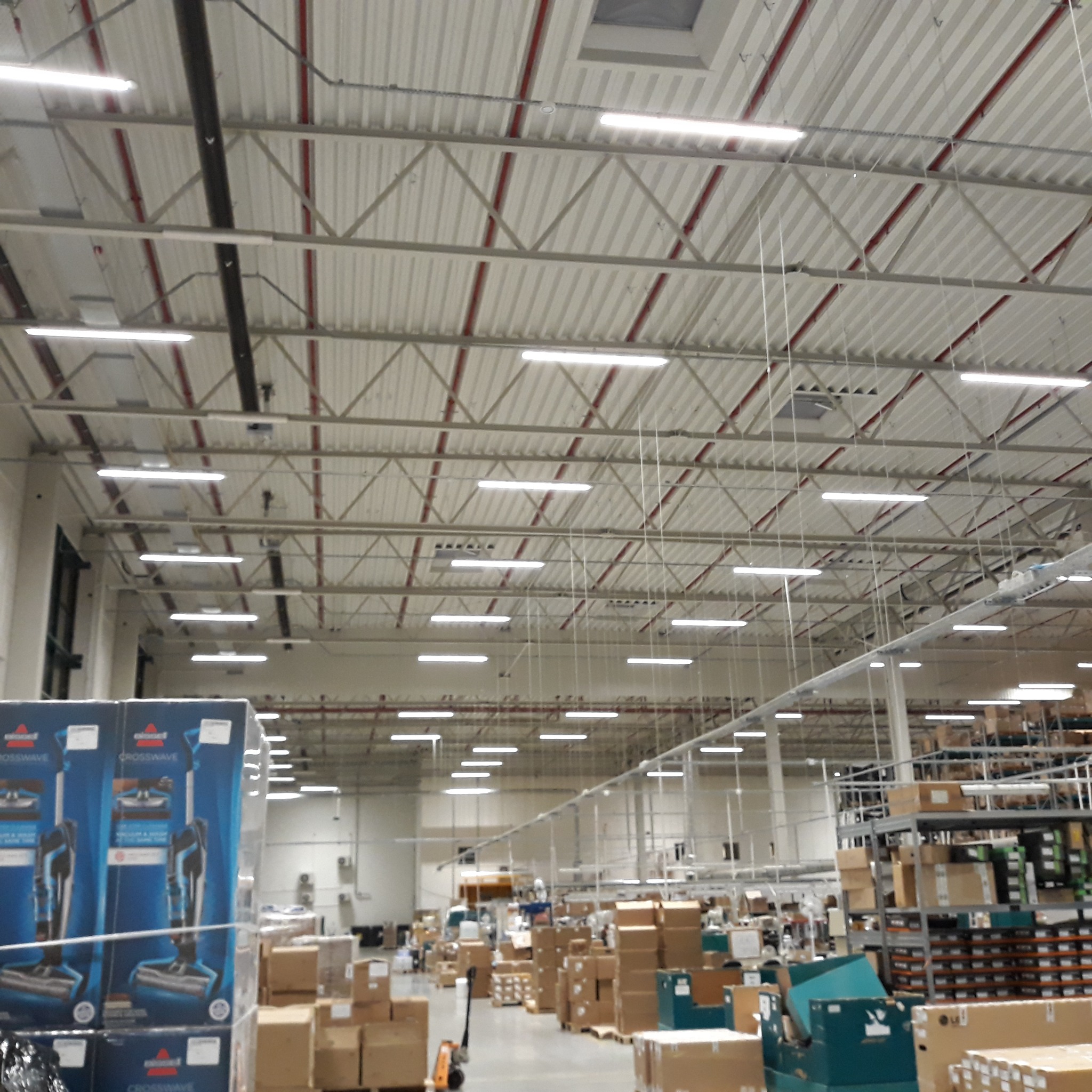 Oświetlenie LED w hali magazynowej z widocznymi elementami konstrukcji dachu i przewodami.