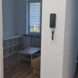 Wnętrze po odświeżeniu ścian w Tychach: białe ściany, drewniana podłoga, widok na pokój z oknem i meblami. Czyste, minimalistyczne wykończenie.