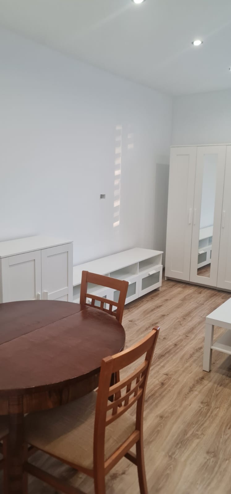 Jasne wnętrze pokoju po odświeżeniu: białe ściany, meble, drewniana podłoga i okrągły stół z krzesłami. Minimalistyczny styl wykończenia.