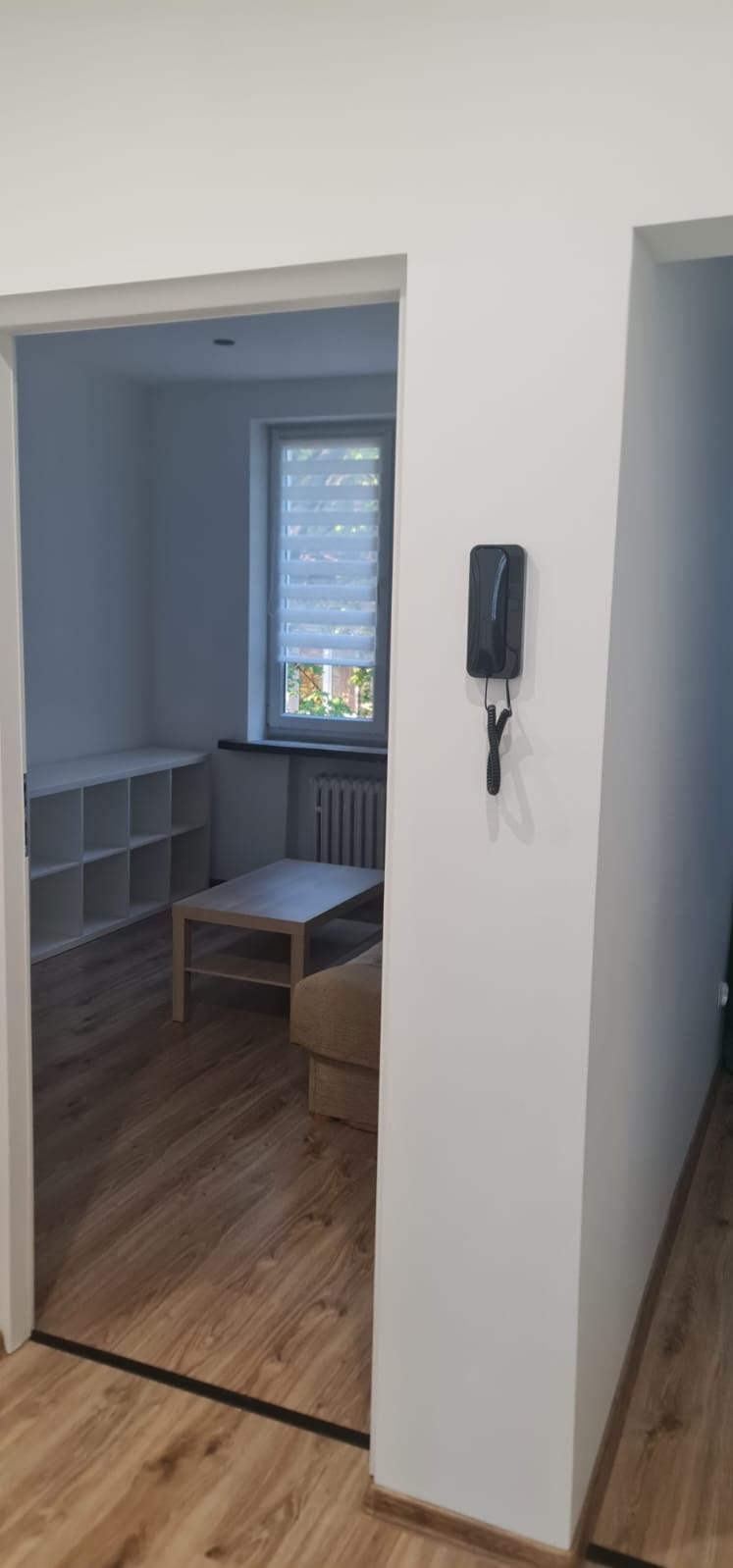 Wnętrze po odświeżeniu ścian w Tychach: białe ściany, drewniana podłoga, widok na pokój z oknem i meblami. Czyste, minimalistyczne wykończenie.