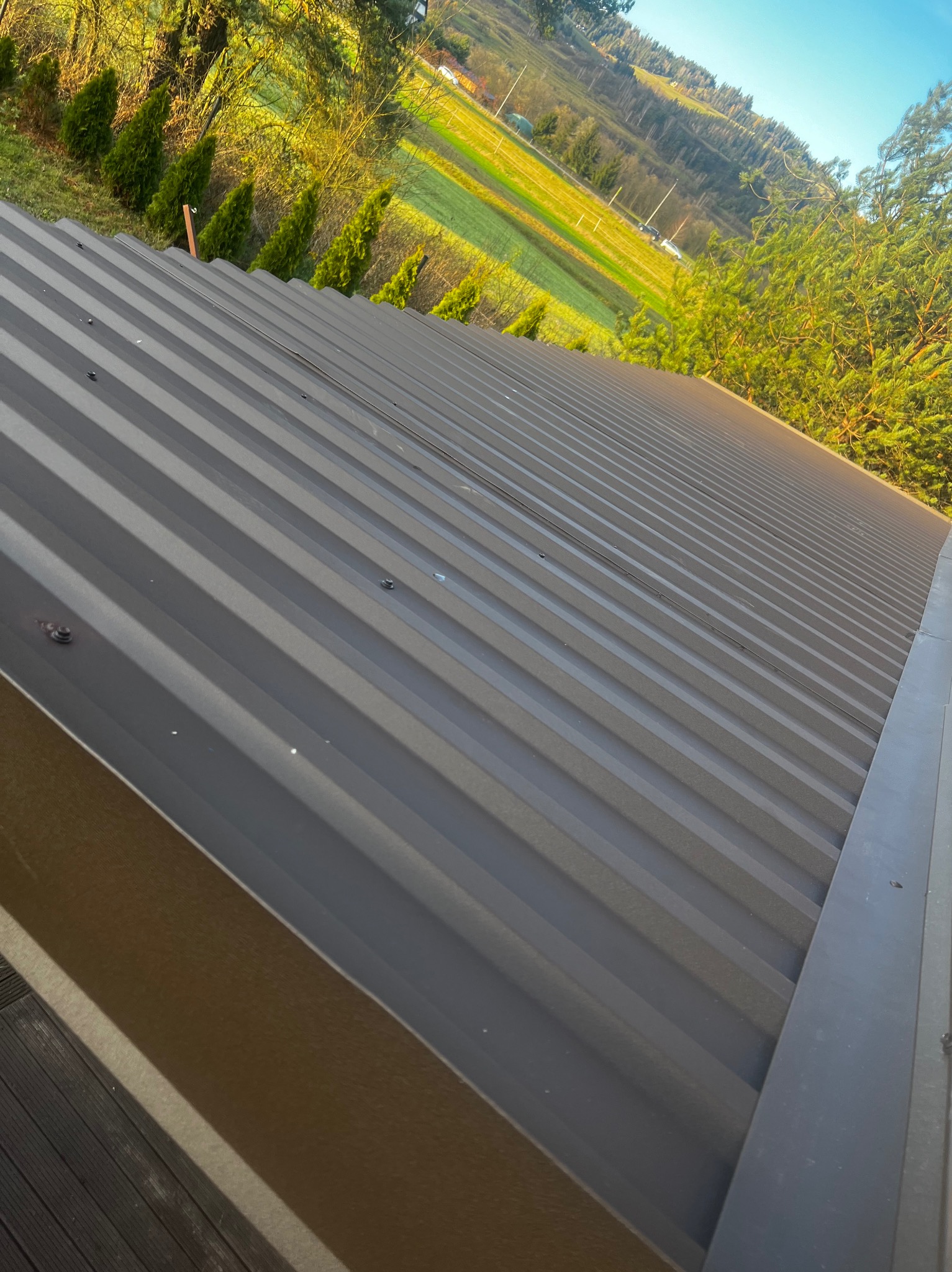 Nowy, brązowy dach z blachy trapezowej z widokiem na zielone wzgórza w Nowym Targu, wykonany w słoneczny dzień.