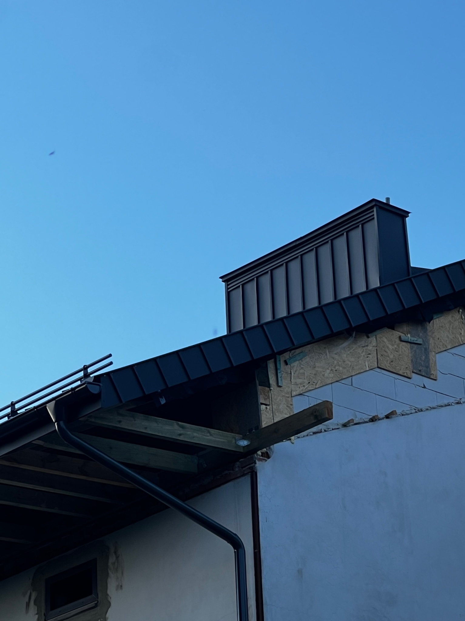 Wymiana dachu z czarnej blachy trapezowej, widoczne elementy konstrukcyjne, komin wentylacyjny i fragment ściany budynku z pustaków.