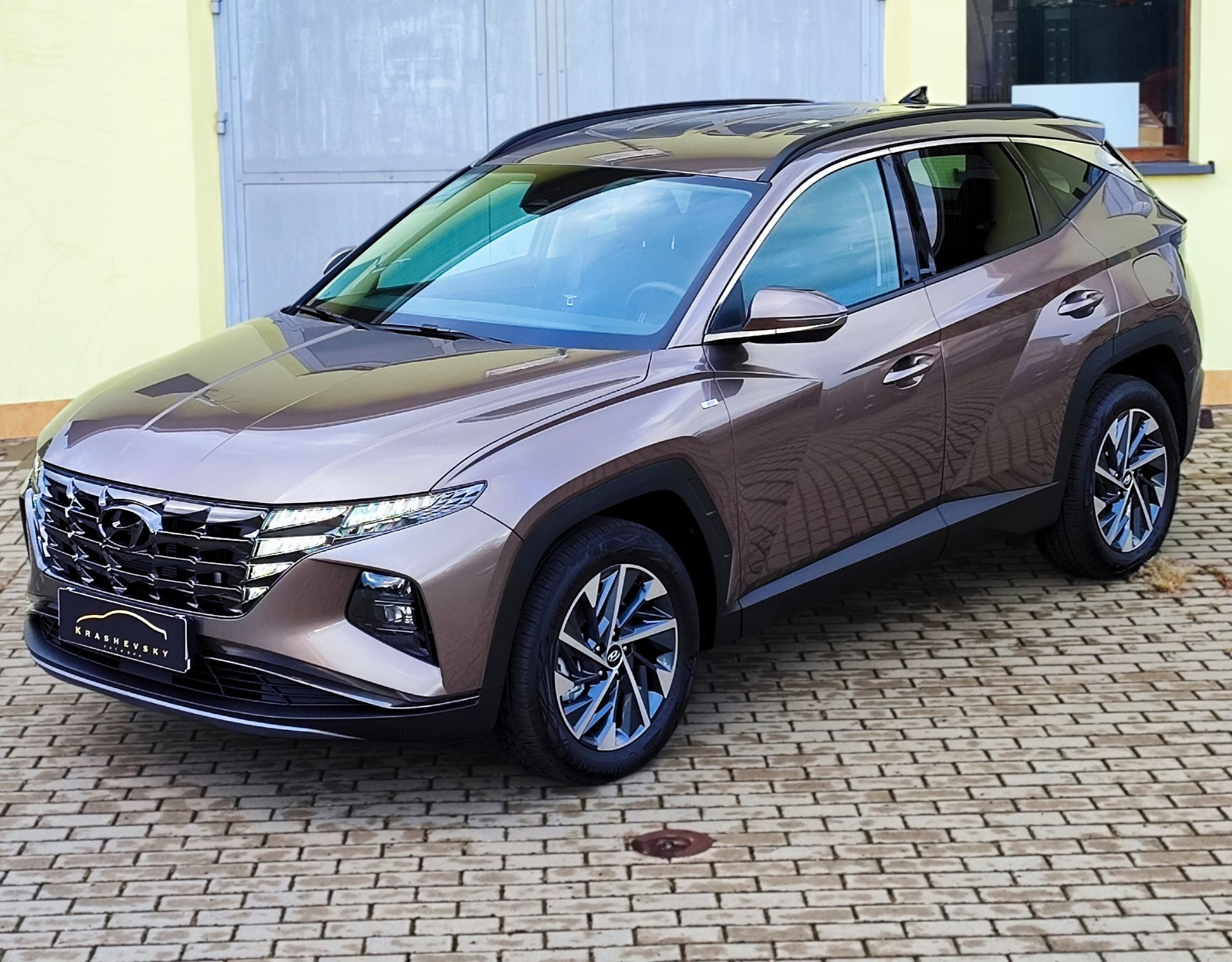 Brązowy Hyundai Tucson po detailingu, widoczny na kostce brukowej przed garażem, z logo Krashevsky Auto Spa na tablicy rejestracyjnej.