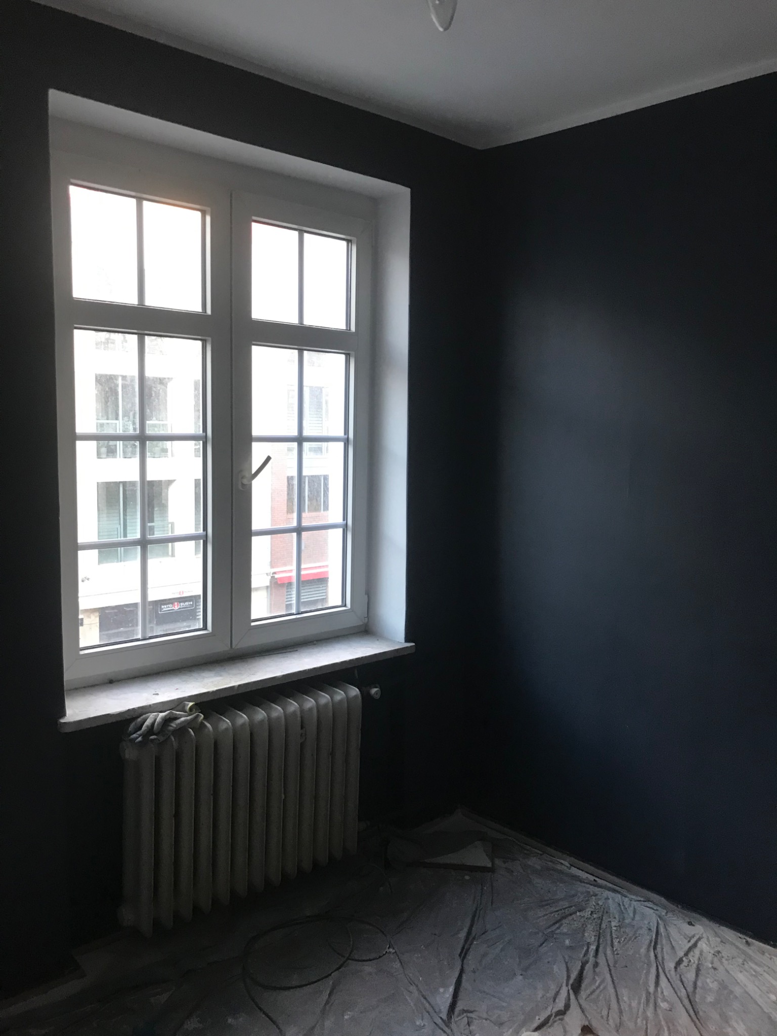 Białe okno PCV w Gdańsku po montażu, widok na budynek z zewnątrz, grzejnik pod oknem przykryty rękawicami roboczymi, ślady prac remontowych na podłodze.