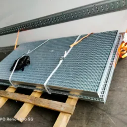 Paleta metalowych krat transportowana wewnątrz busa, zabezpieczona pasami i umieszczona na drewnianych legarach.