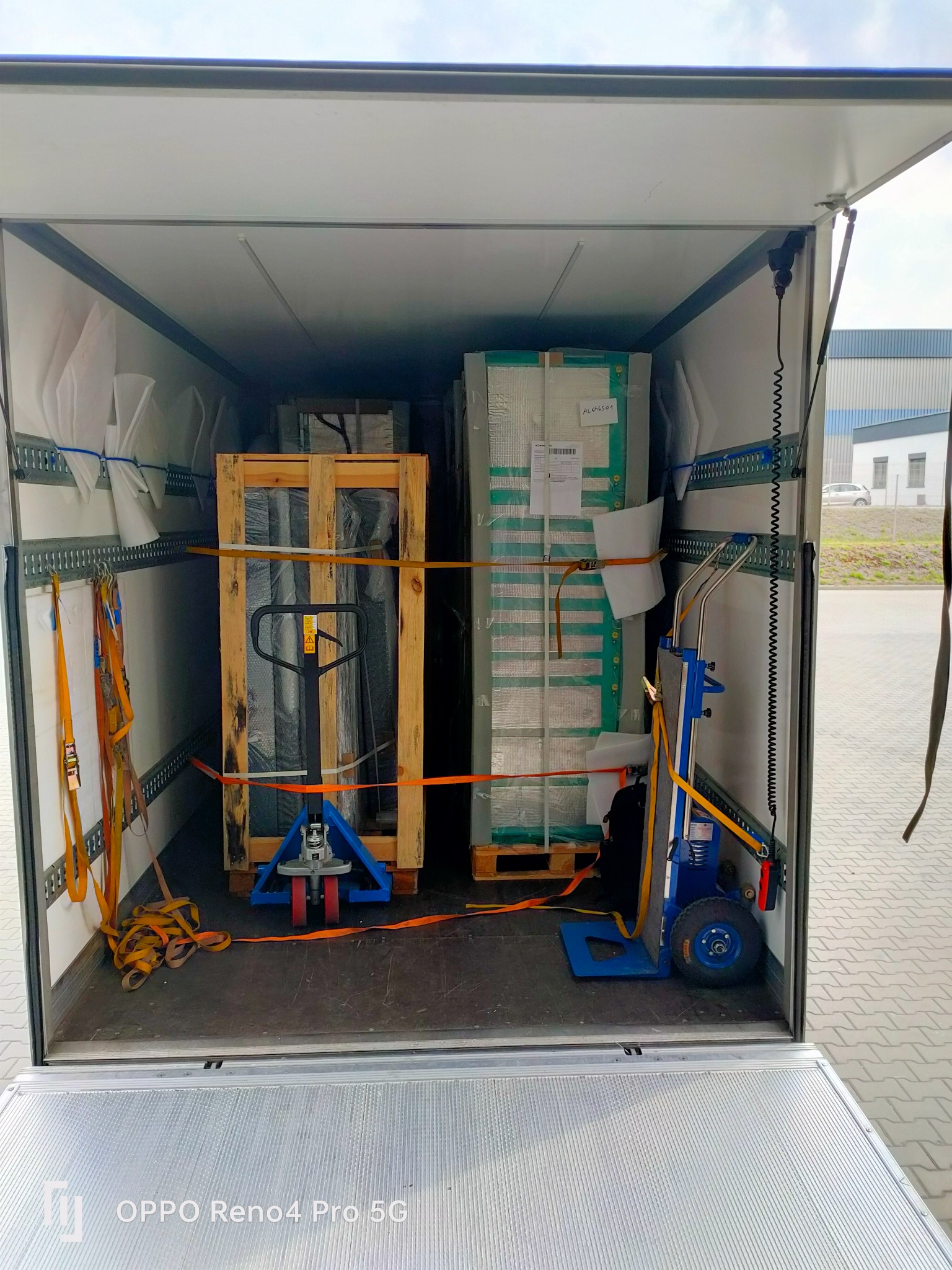 Wnętrze otwartego busa transportowego z paletami zabezpieczonymi pasami, wózki paletowe wewnątrz, widoczne elementy mocujące na ścianach.