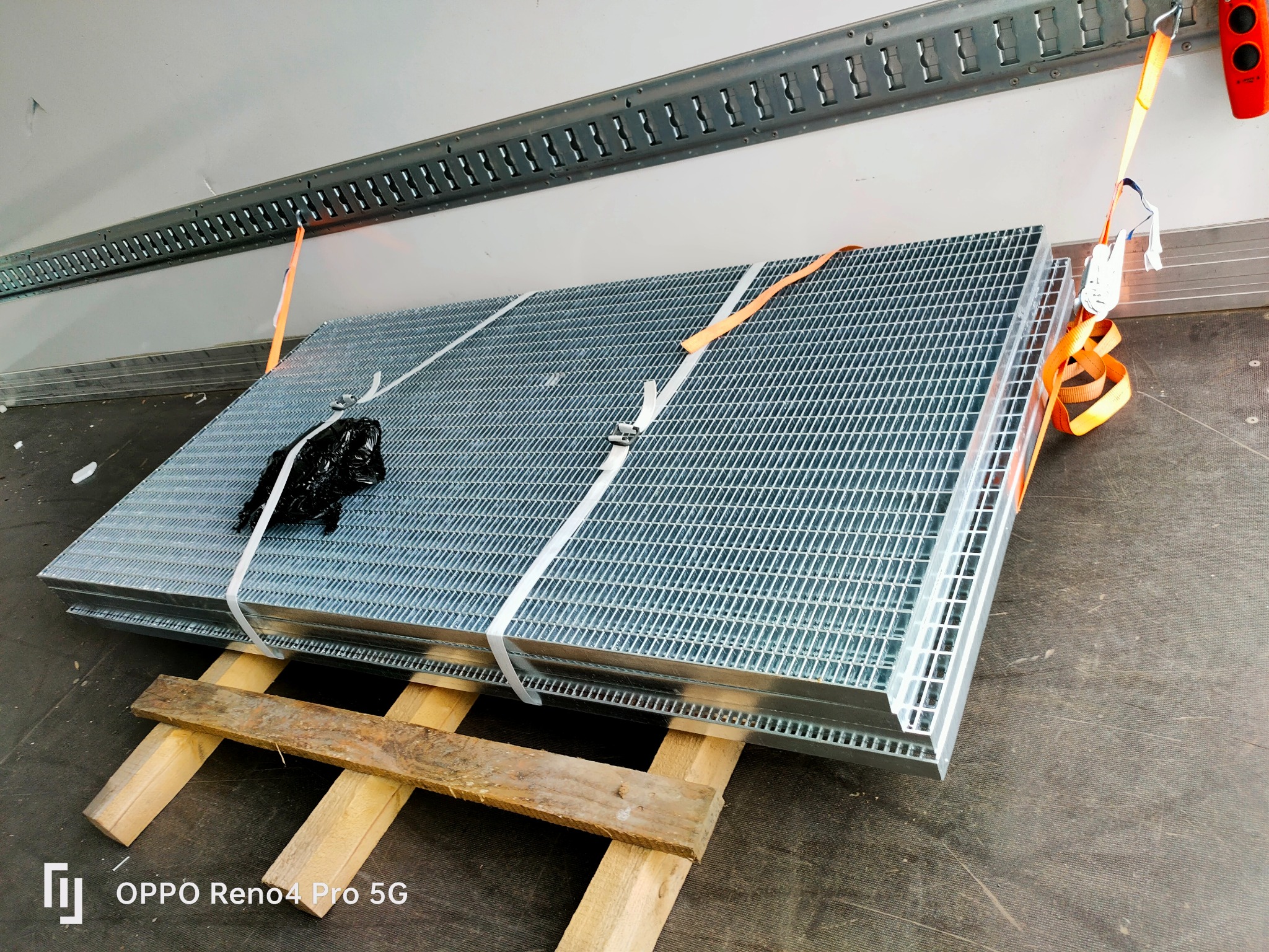 Paleta metalowych krat transportowana wewnątrz busa, zabezpieczona pasami i umieszczona na drewnianych legarach.