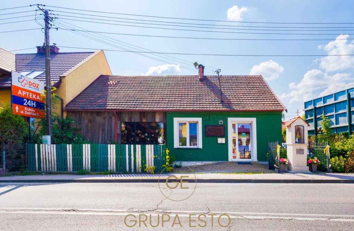 Niski, zielony budynek z brązowym dachem, z szyldem 'Bospor Kuchnia', widoczny z ulicy w słoneczny dzień.