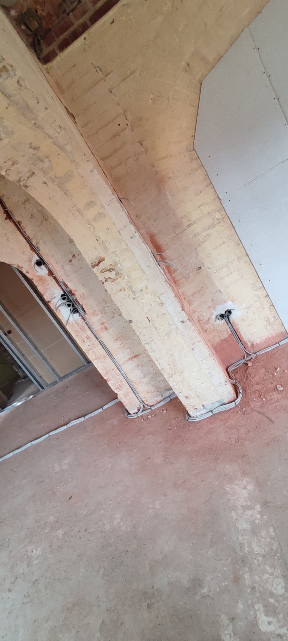 Wnętrze w trakcie remontu z widocznymi przewodami elektrycznymi prowadzonymi po ceglanych łukach sufitu i ścianie, widoczne puszki instalacyjne.