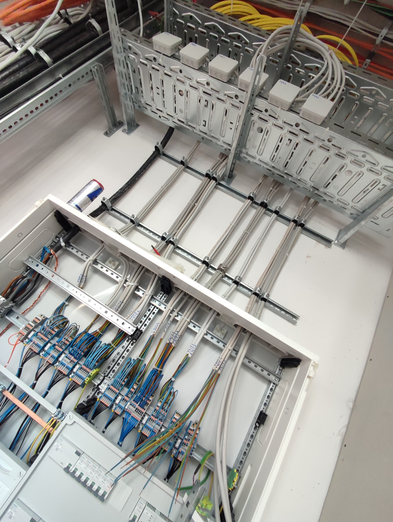 Rozdzielnica elektryczna z podłączonymi przewodami, widoczne kable w korytkach montażowych i puszki instalacyjne, etykiety na kablach z opisem obwodów.