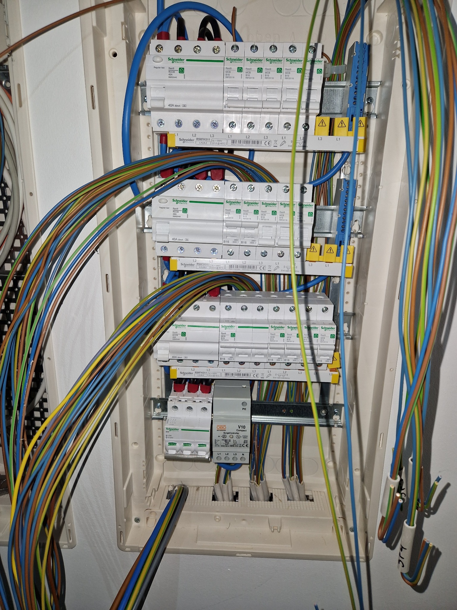 Rozdzielnia elektryczna w trakcie montażu, widoczne liczne przewody w różnych kolorach, zabezpieczenia marki Schneider Electric, oraz elementy montażowe w białej obudowie.