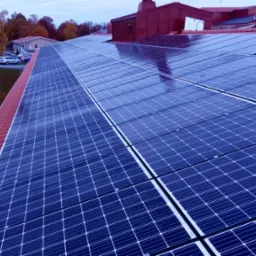 Rząd paneli słonecznych na czerwonym dachu domu jednorodzinnego, widoczne krople deszczu na panelach, drzewa w tle.