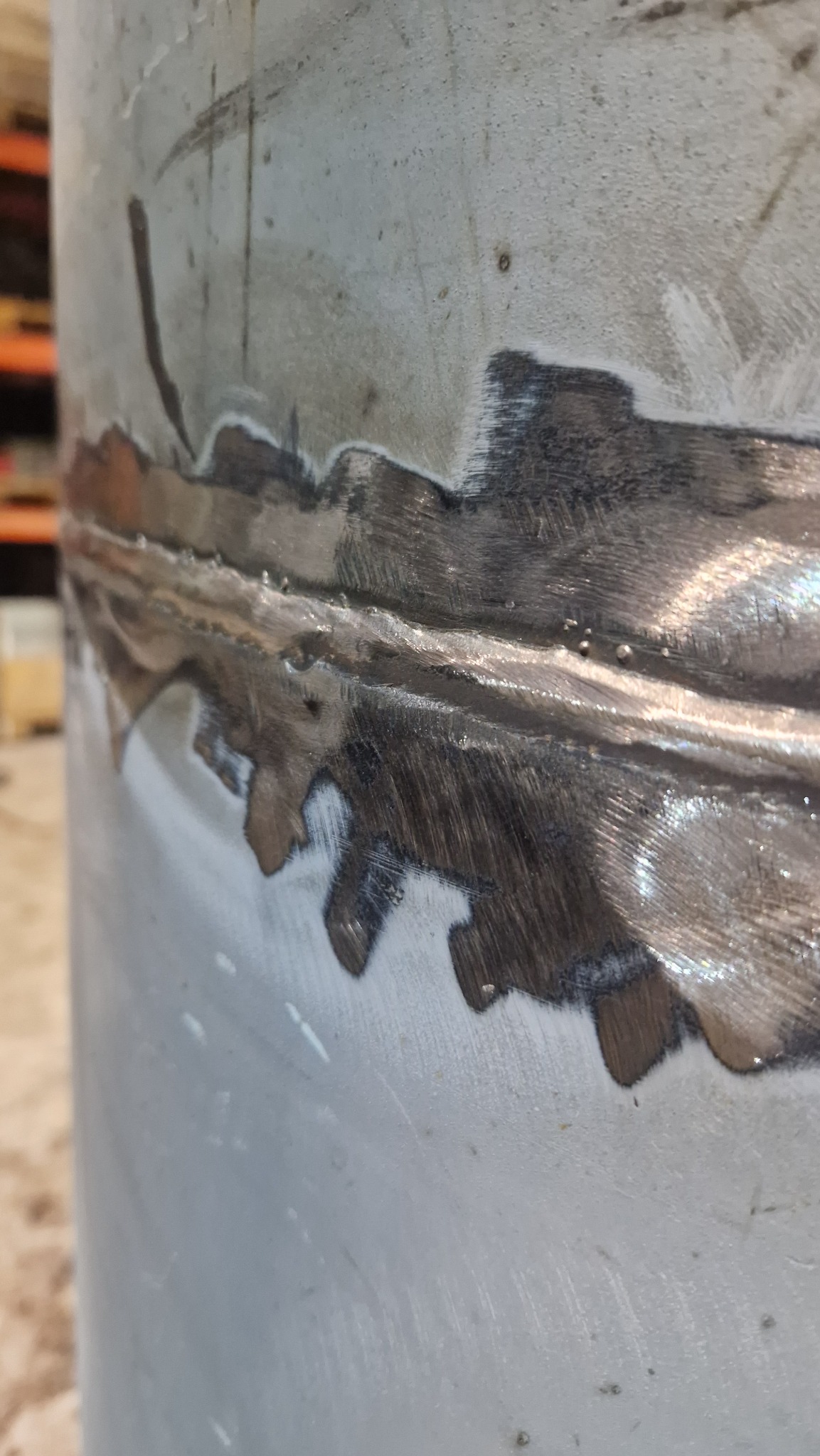 Szlifowana spoina na okrągłym, metalowym elemencie konstrukcyjnym, widoczne ślady obróbki i niewielkie nierówności powierzchni.