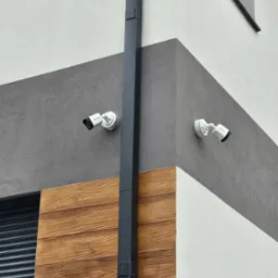 Dwie kamery monitoringu Hikvision zamontowane na elewacji budynku z drewnianą okładziną i szarą strefą. Widoczna rynna pionowa.