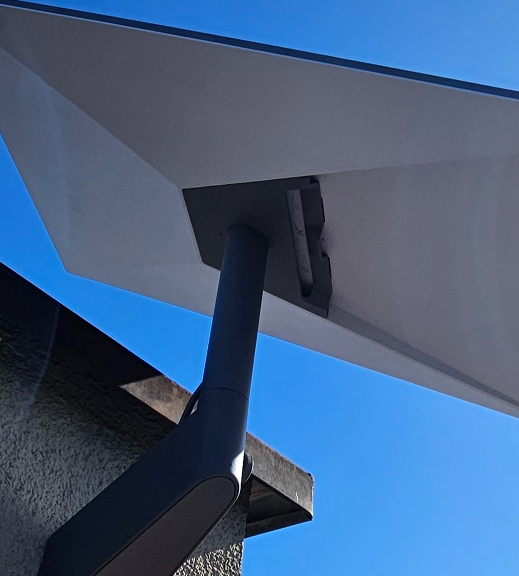 Antena Starlink zamontowana na ścianie budynku, widok z dołu na tle błękitnego nieba. Szara obudowa i biała powierzchnia anteny. Kąt ujęcia podkreśla nowoczesny design.