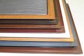 Stos różnych typów ramek moskitier w kolorach drewna, brązu, bieli i szarości, ułożonych jedna na drugiej na białym tle.