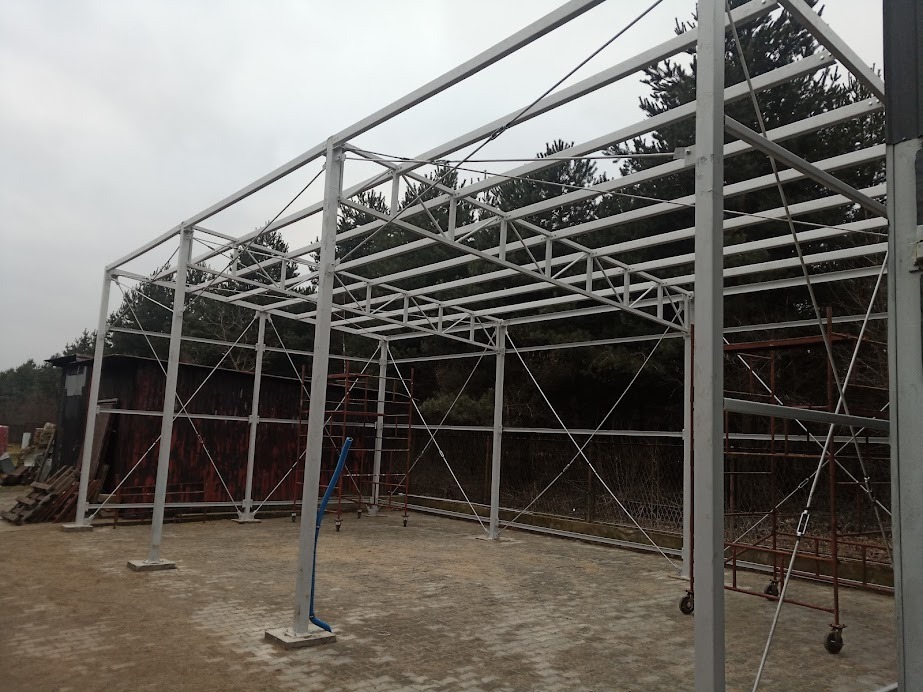 Konstrukcja stalowa z profili zamkniętych, przygotowana do dalszej zabudowy, widoczne rusztowania i drzewa w tle.