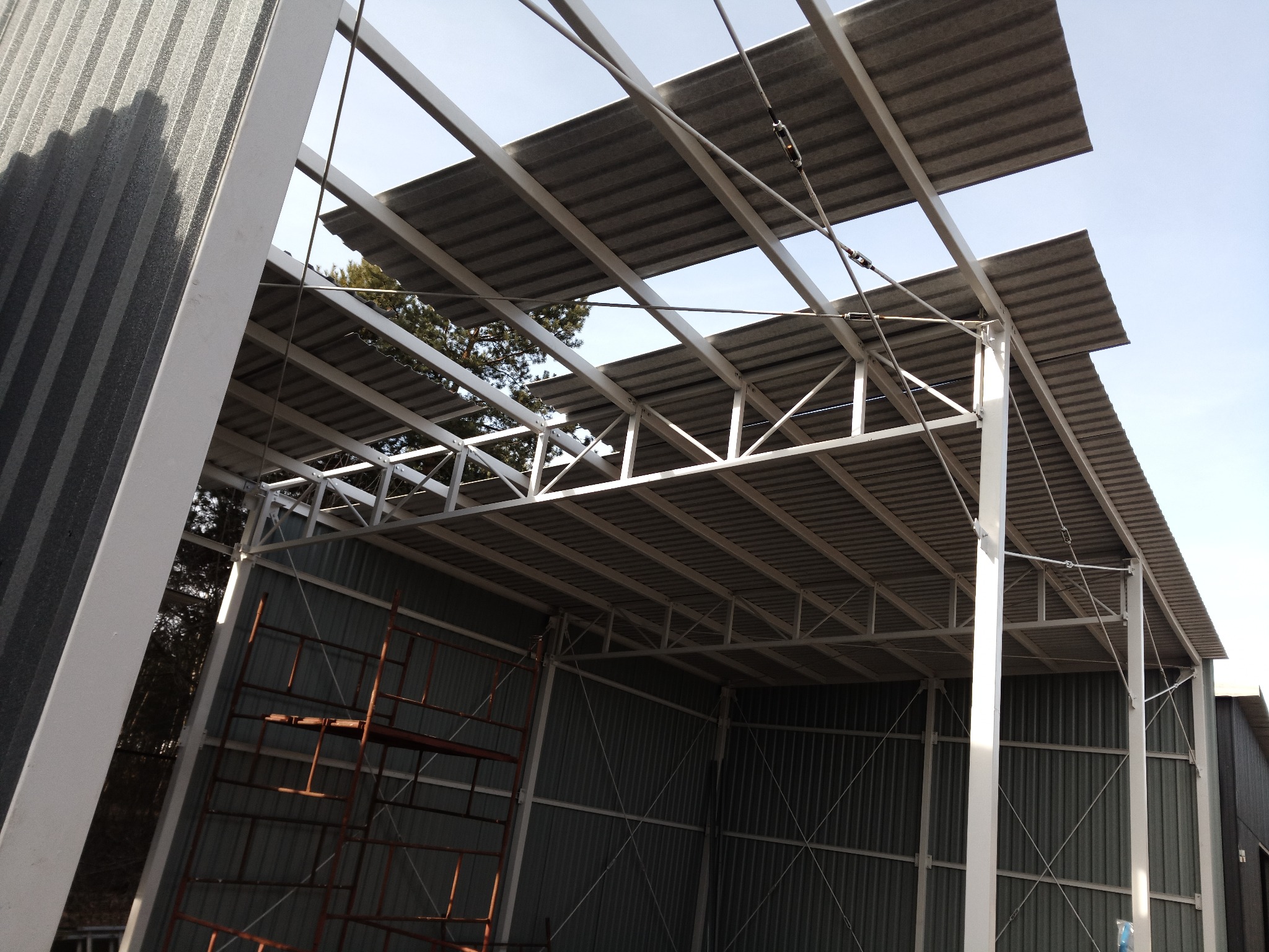 Konstrukcja stalowa z blachy falistej w trakcie montażu, widoczne rusztowania i elementy mocujące.