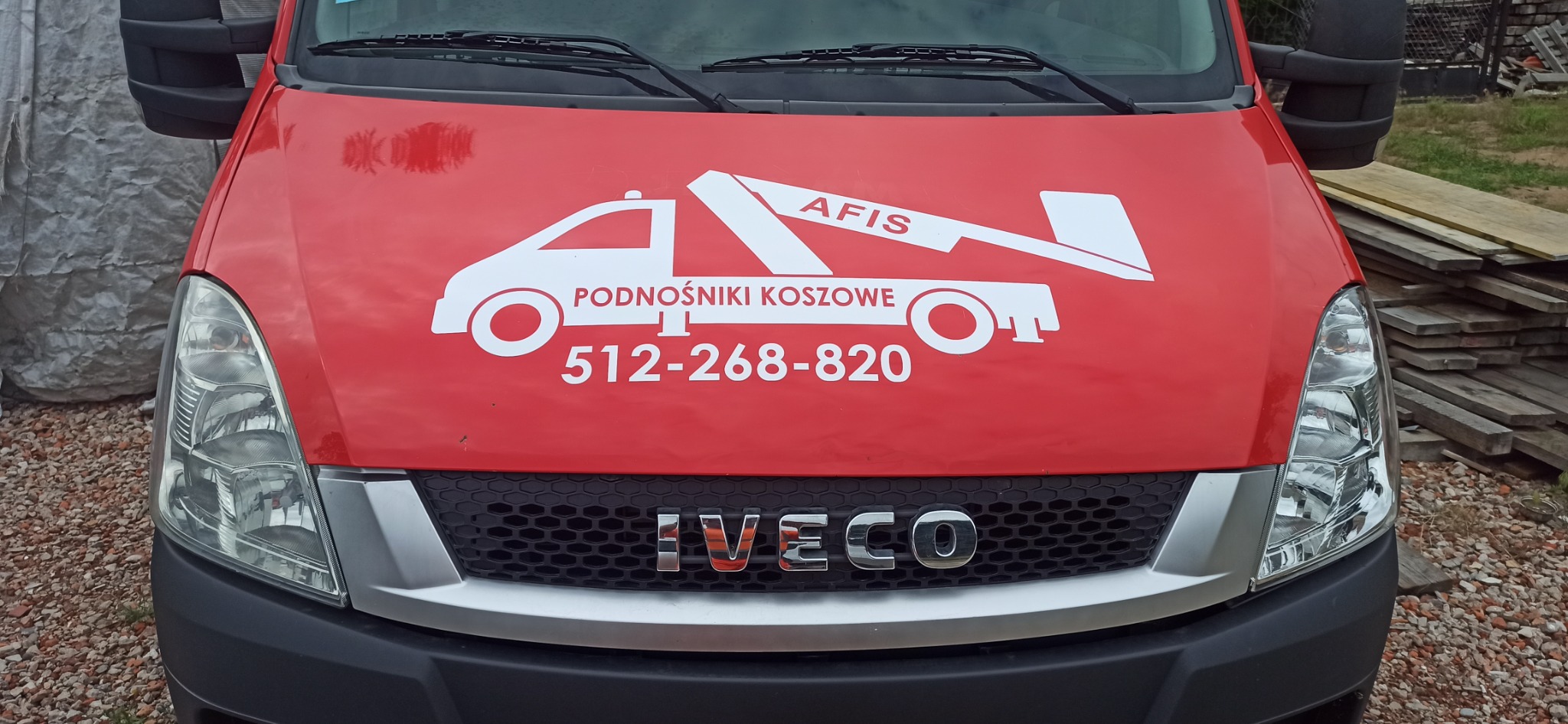Czerwony samochód dostawczy marki Iveco z białym logo firmy AFIS Podnośniki Koszowe i numerem telefonu 512-268-820 na masce.
