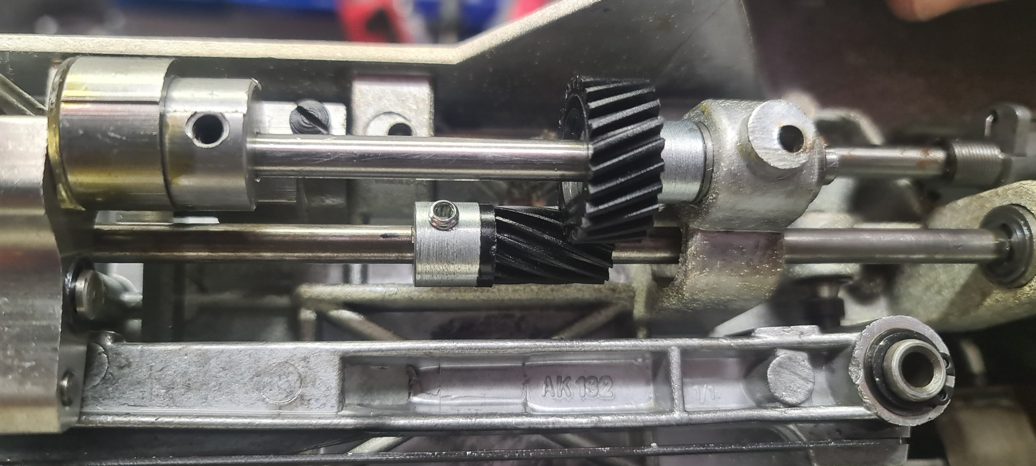 Wnętrze maszyny z widocznymi przekładniami zębatymi, wałami i elementami mocującymi; widoczny numer AK 192 na metalowej obudowie.