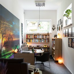 GABINET WSPARCIA I ROZWOJU HIPNOODNOWA DAMIAN STANIEK - Jasne wnętrze gabinetu z biurkiem, regałami i dekoracjami, w tym solne lampy i obraz drzewa na ścianie. Przytulna przestrzeń do sesji relaksacyjnych.