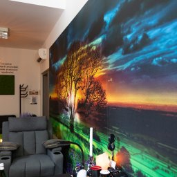 GABINET WSPARCIA I ROZWOJU HIPNOODNOWA DAMIAN STANIEK - Przytulne wnętrze gabinetu z fotelem relaksacyjnym i fototapetą z motywem drzewa na tle zachodu słońca, tworzące atmosferę spokoju i odprężenia.