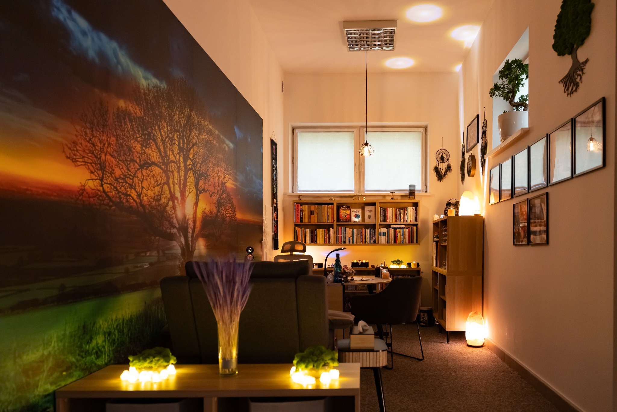 Klimatyczne wnętrze gabinetu z fototapetą drzewa, regałem książek i solnymi lampami. Stonowana kolorystyka i przytulne oświetlenie tworzą relaksującą atmosferę.
