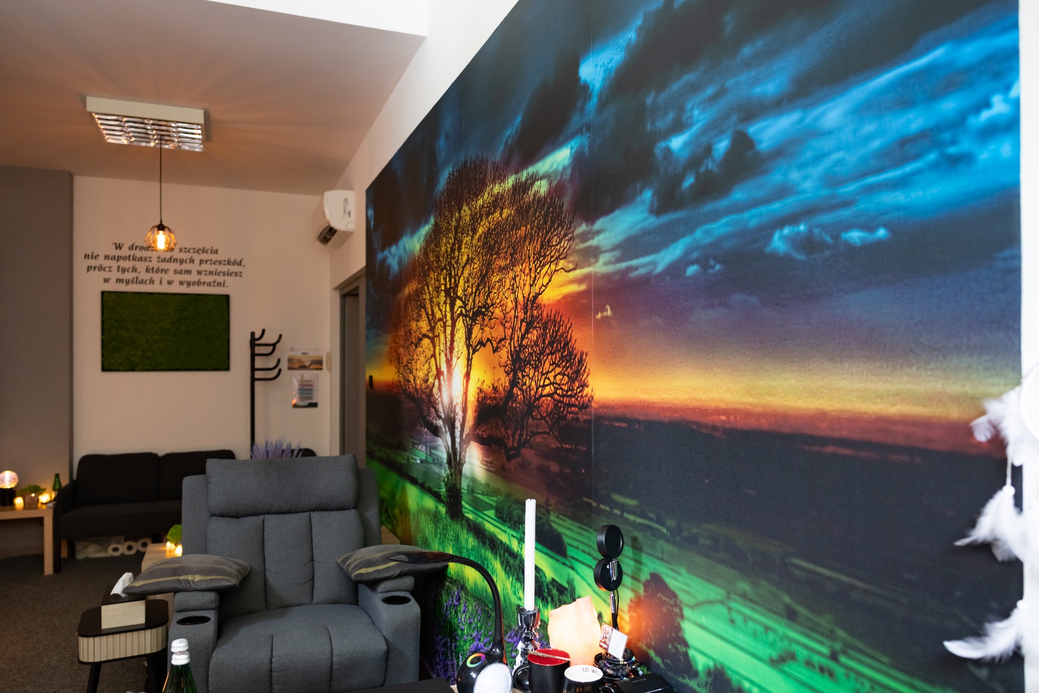 Przytulne wnętrze gabinetu z fotelem relaksacyjnym i fototapetą z motywem drzewa na tle zachodu słońca, tworzące atmosferę spokoju i odprężenia.