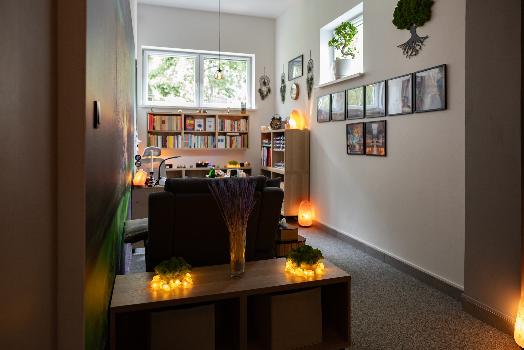 Przytulne wnętrze gabinetu z biblioteczką, dekoracjami, lampami solnymi i roślinami, tworzące relaksującą atmosferę. Wazon z suszem na pierwszym planie.