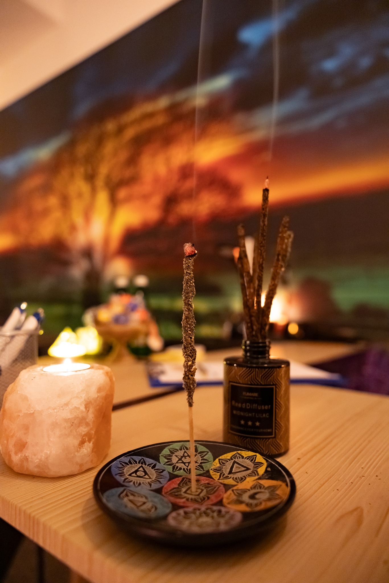Aromatyczny seans: palący się kadzidło na ozdobnym talerzyku z symbolami, obok świeca solna i dyfuzor zapachowy, tworzące relaksującą atmosferę.