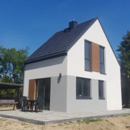 Nowoczesny dom jednorodzinny z dwukolorową elewacją (biało-szarą), ciemną dachówką i drewnopodobnymi żaluzjami, otoczony zielenią i zadaszoną huśtawką ogrodową na kostce brukowej.