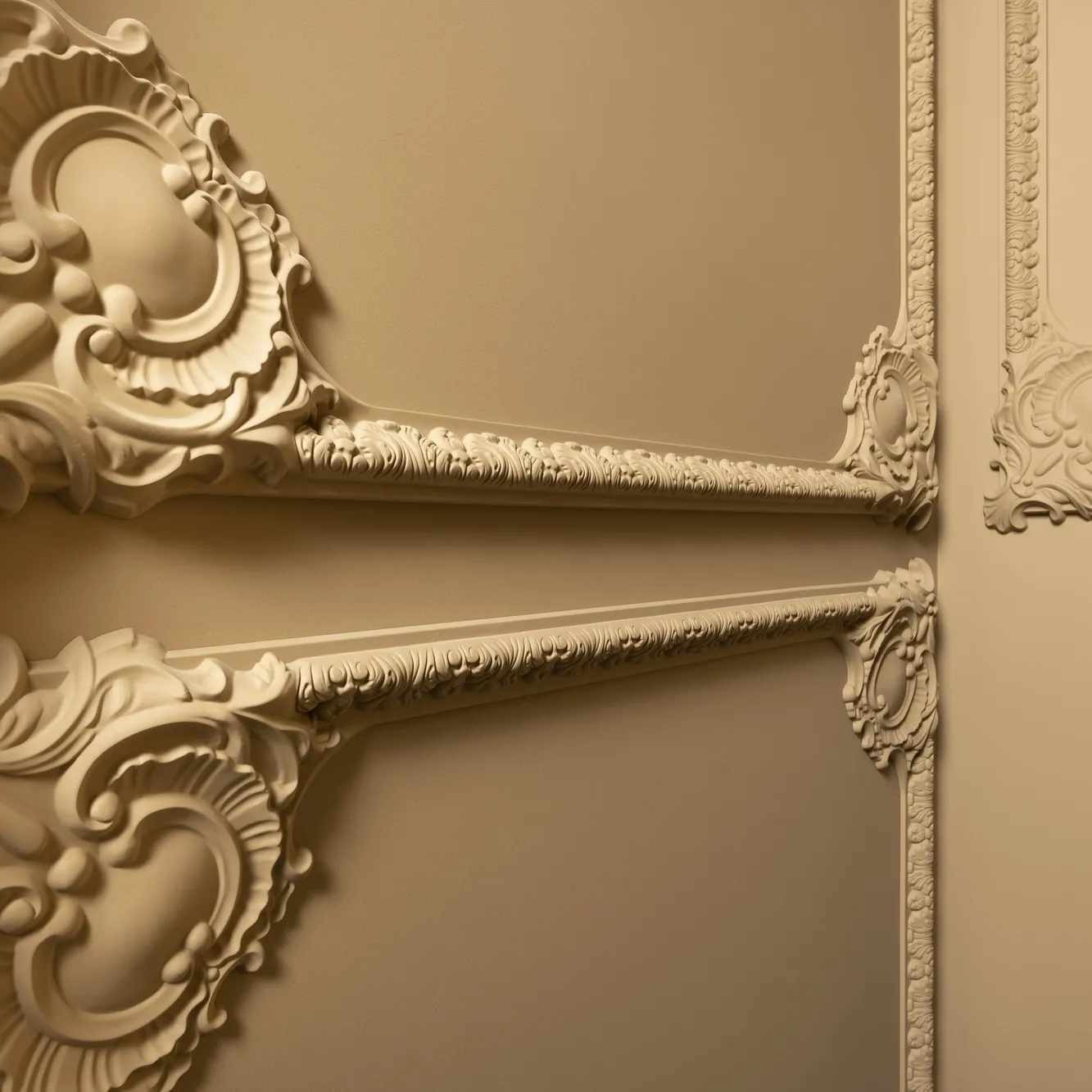 Dekoracyjne listwy przysufitowe i ścienne z gipsu, kremowe, z ornamentami w stylu klasycznym, zamontowane na ścianie w kolorze beżowym.