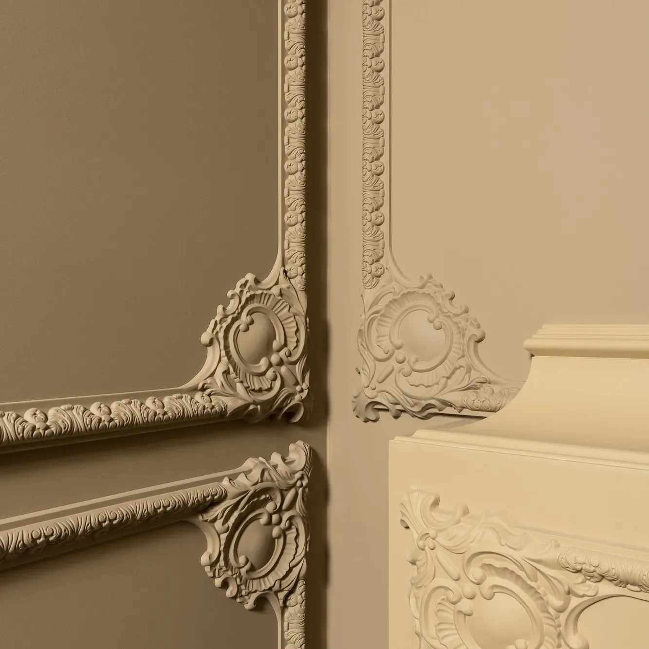 Fragment dekoracyjnej sztukaterii narożnej w kremowym odcieniu, zdobiącej ścianę w kolorze taupe, z detalami roślinnymi i ornamentami w stylu klasycystycznym.