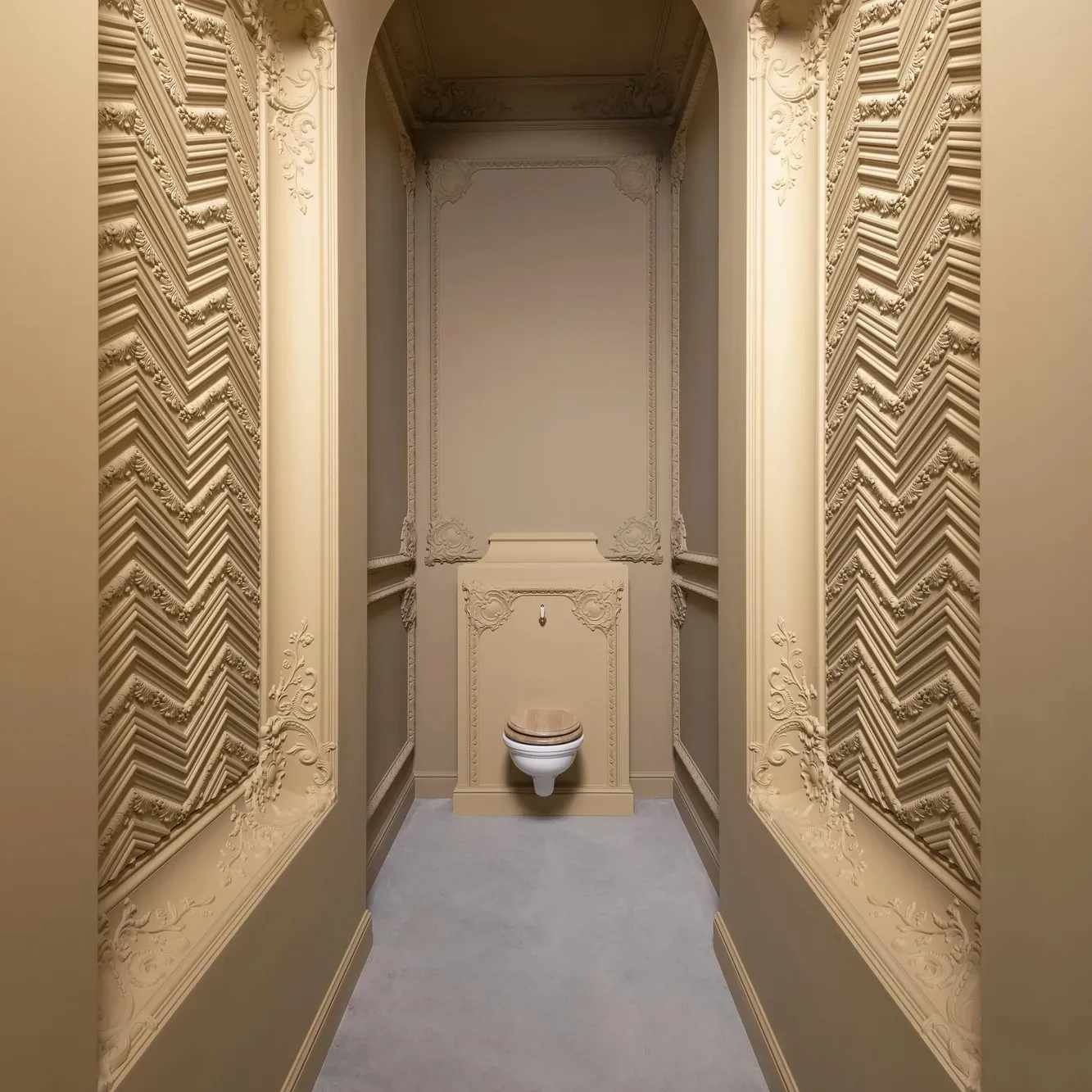 Beżowa toaleta w stylu retro z ozdobnymi sztukateriami na ścianach, widok z perspektywy korytarza.