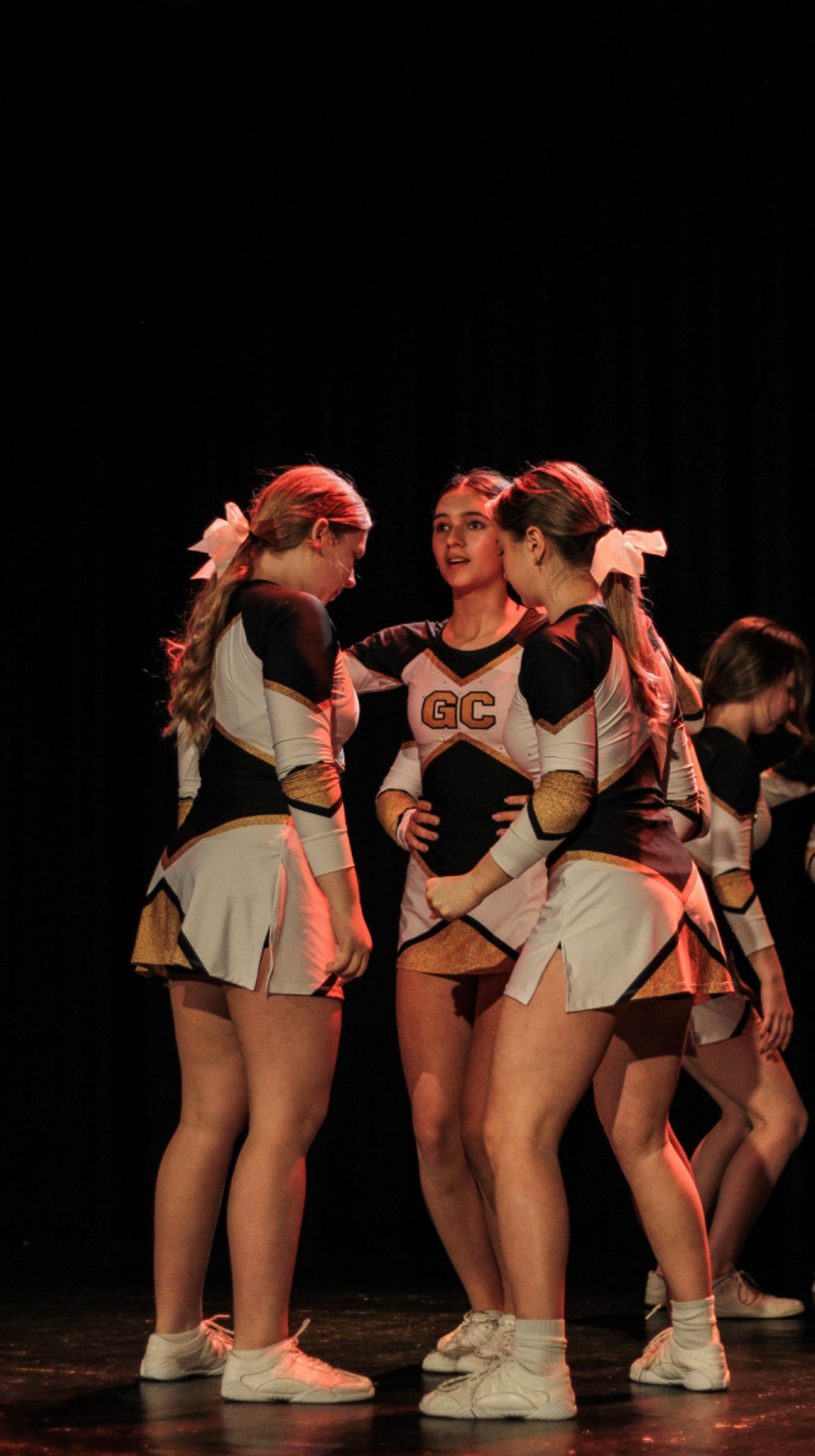 Grupa cheerleaderek w strojach z literami 'GC' w Nowym Sączu, rozmawiających przed występem na czarnym tle sceny, oświetlonych czerwonym światłem.