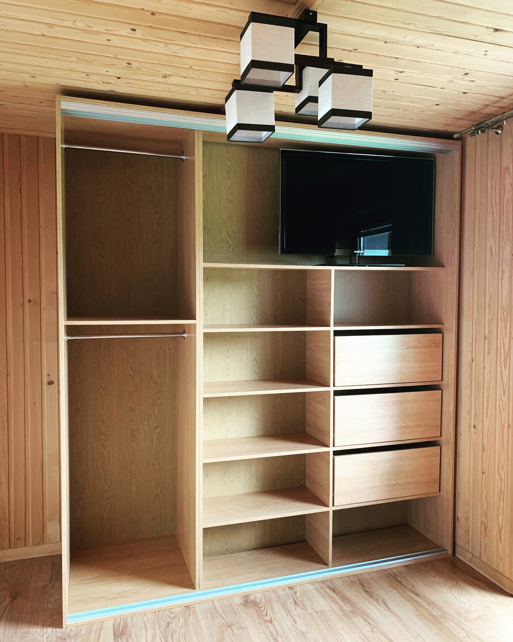Zabudowa garderoby z drewna w Ząb z telewizorem, oświetleniem i szufladami, widok na półki i drążki na ubrania.