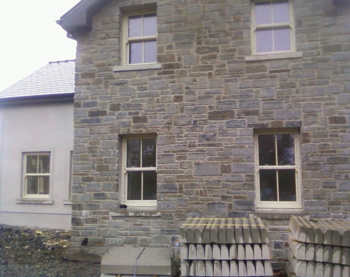 Elewacja budynku z kamienia naturalnego z oknami w jasnych ramach. Na pierwszym planie ułożone elementy wykończeniowe.