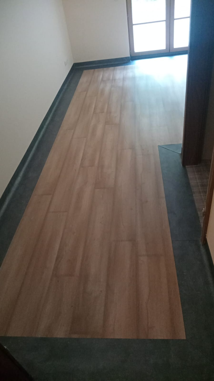 Jasne panele podłogowe z ciemnoszarą listwą przypodłogową w świeżo wyremontowanym pokoju z oknem.