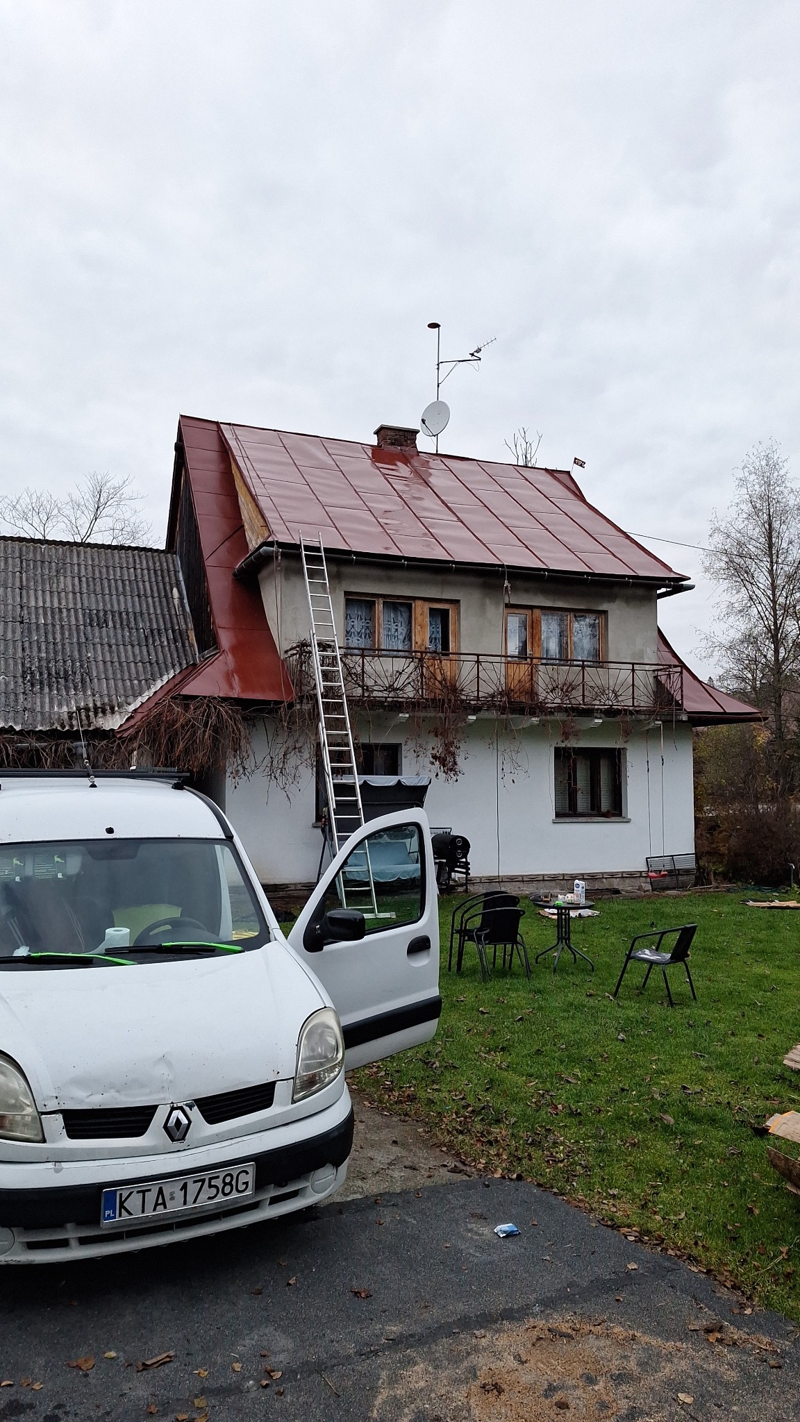Dom z nowym, czerwonym dachem, z przystawioną drabiną. Obok zaparkowany biały samochód dostawczy z otwartymi drzwiami.